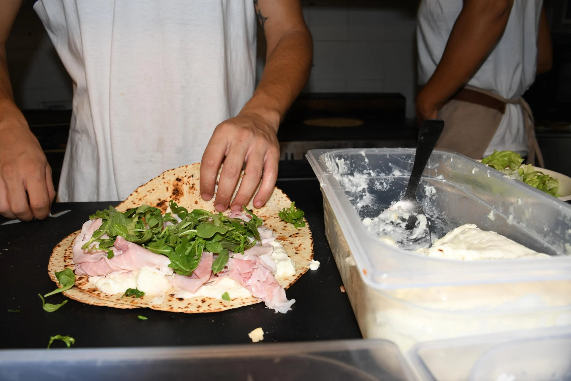 La farcitura a mano di una piadina nel laboratorio di MÈNSA